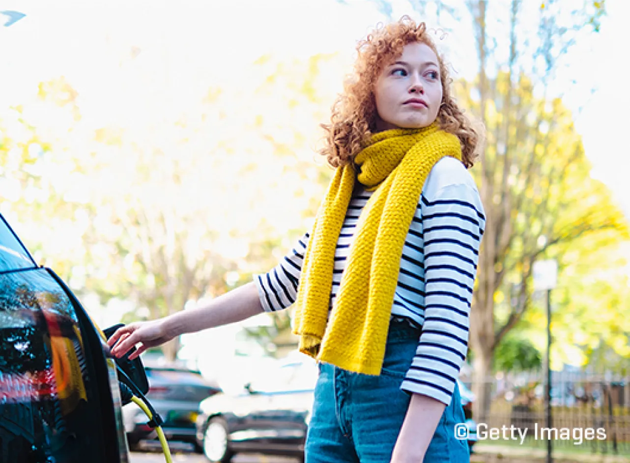 Une femme avec un foulard jaune recharge une voiture électrique